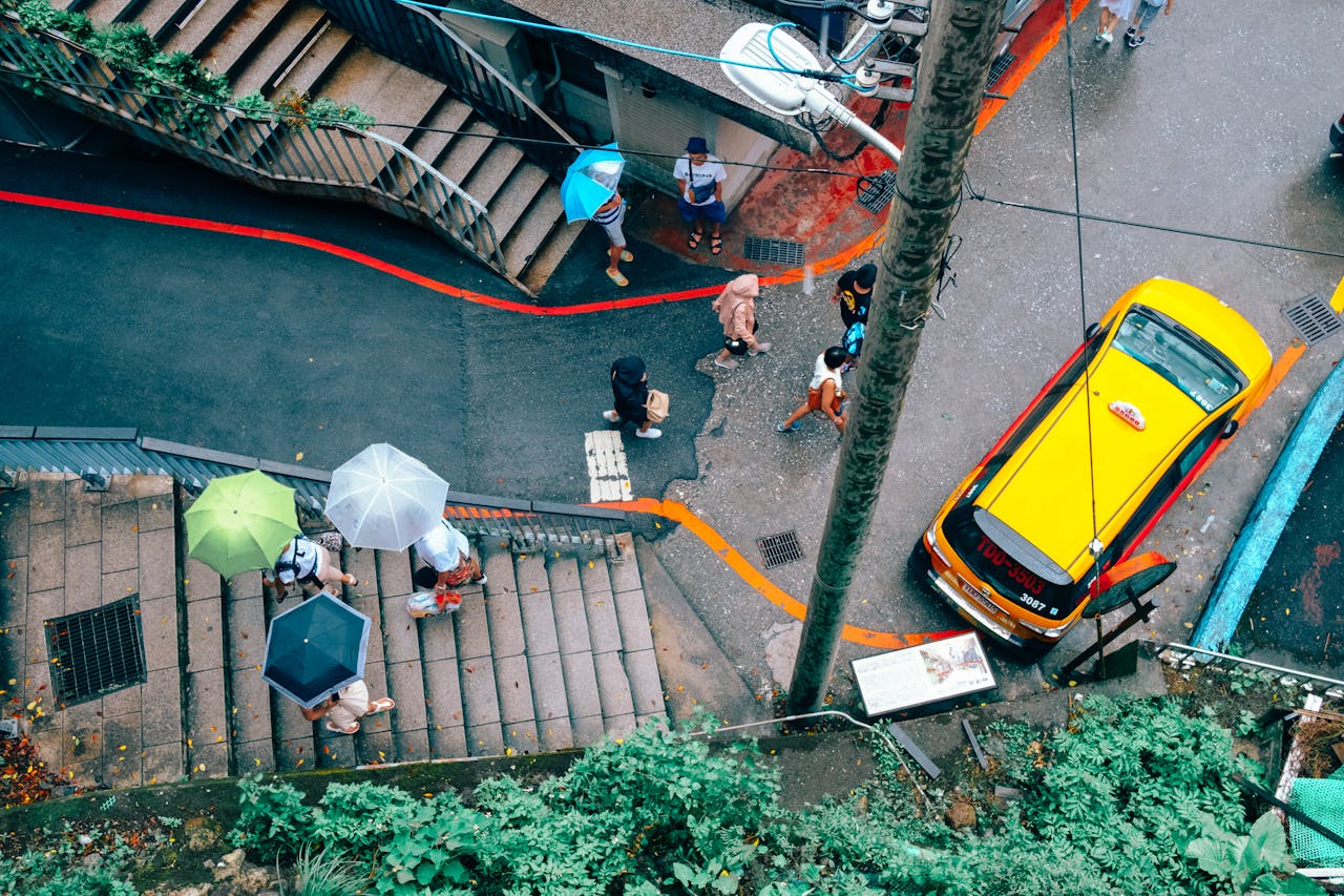 An aerial view capturing people with umbrellas walking near a taxi in Taipei's Xinyi District.
